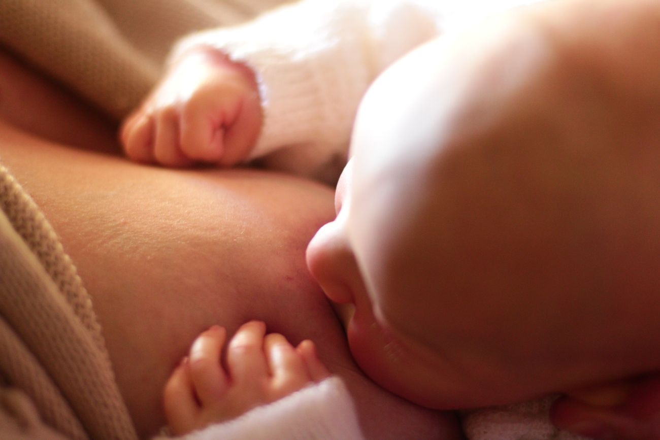 A parent's hand gently holding their baby's hand