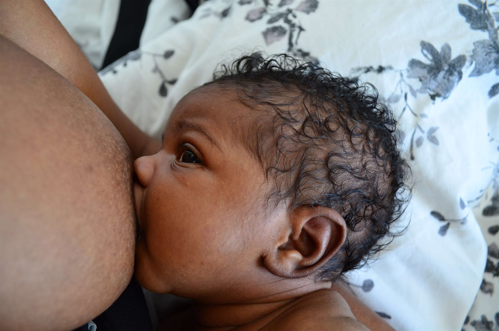A baby breastfeeding, latched and gazing up at their parent