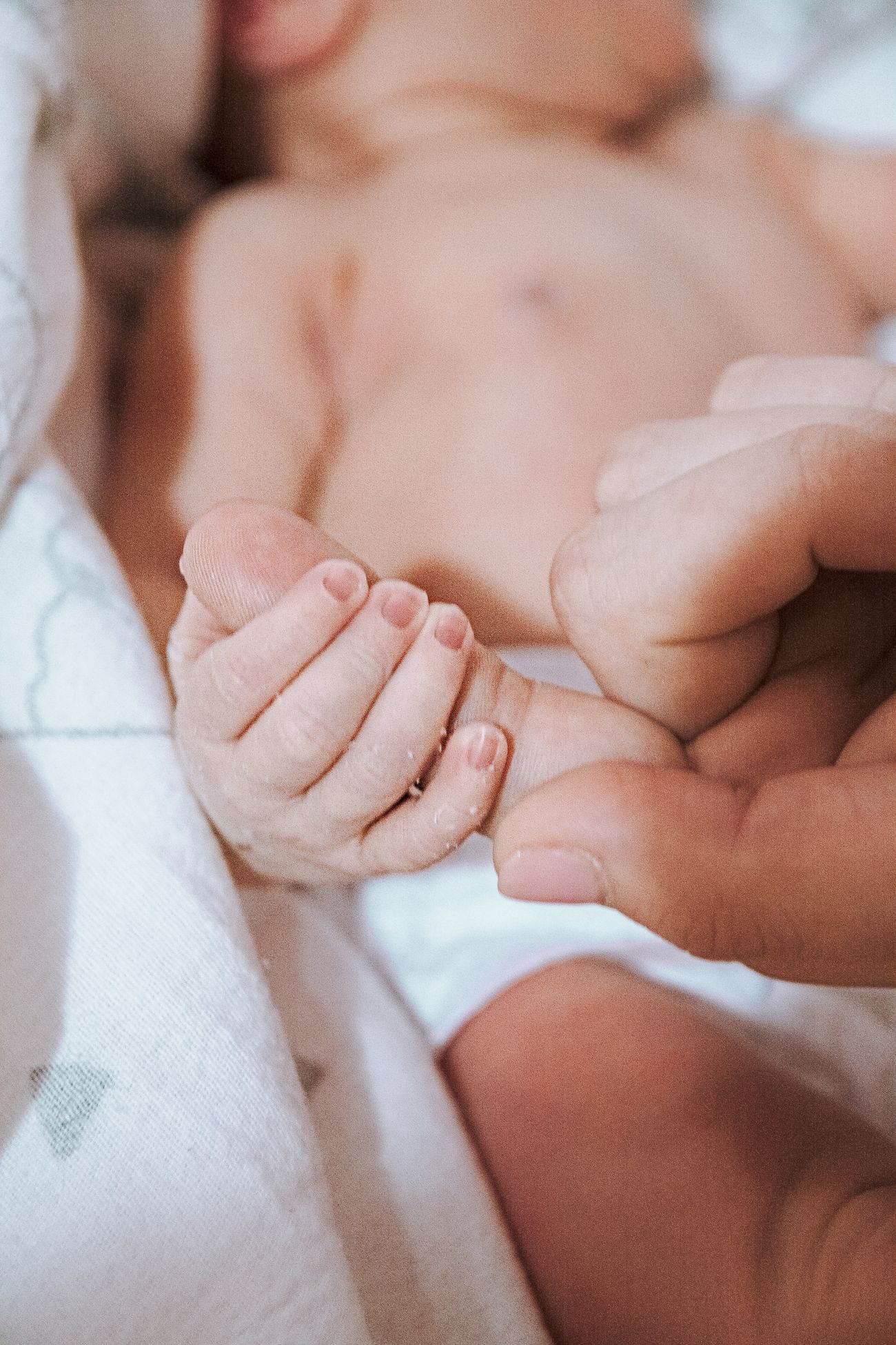 A newborn's hand gently gripping a parent's finger